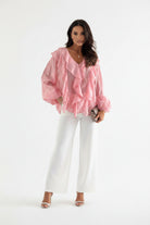 Woman wearing a pink ruffled blouse with a blurred indoor background