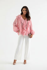 Woman wearing a pink ruffled blouse with a blurred indoor background