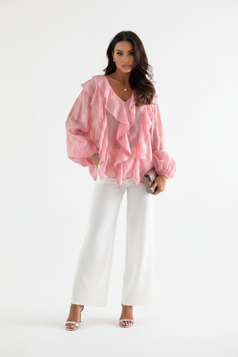 Woman wearing a pink ruffled blouse with a blurred indoor background