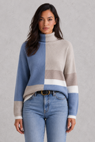 Woman wearing a color-blocked sweater and jeans against a gray background