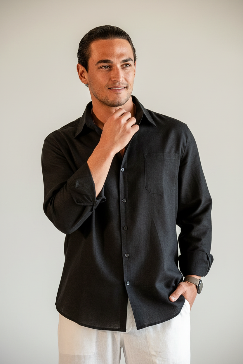Man wearing a black shirt and white pants standing in a room with a lamp and plant.