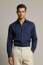 Man wearing a blue shirt and sunglasses in an outdoor setting with buildings and trees.