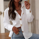 Woman wearing a white blazer with gold buttons and blue jeans indoors.