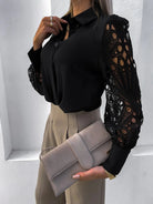 Person wearing a black blouse with sheer sleeves holding a beige clutch against a white background