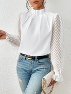 Person wearing a white blouse with sheer sleeves and light blue jeans against a white background