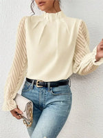 Woman wearing a cream blouse with long sleeves and blue jeans against a white background