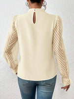 Beige blouse with long sleeves and cut-out back design worn by a person against a white wall.