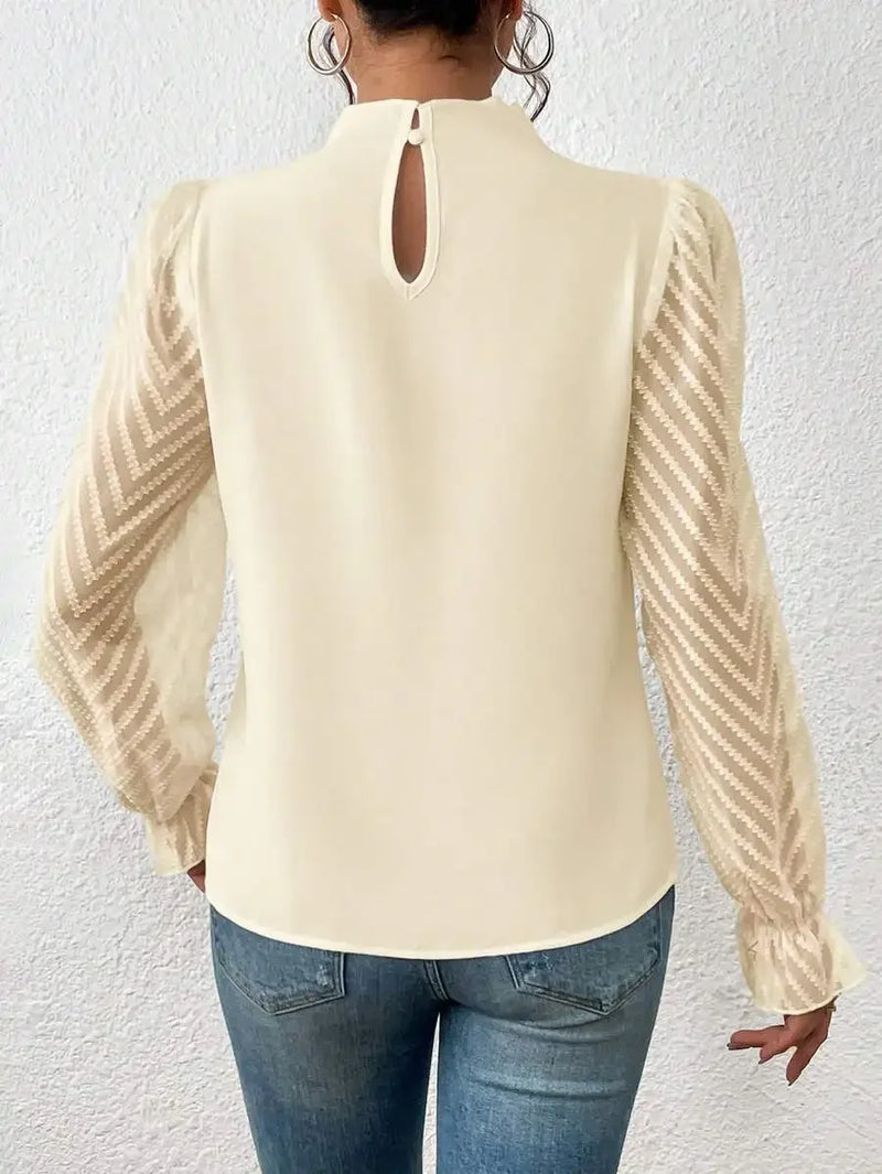 Beige blouse with long sleeves and cut-out back design worn by a person against a white wall.