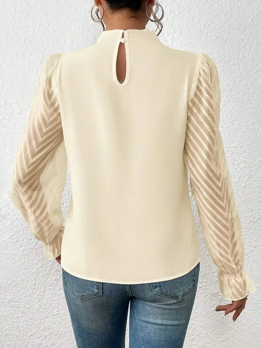 Beige blouse with long sleeves and cut-out back design worn by a person against a white wall.