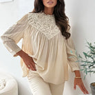 Woman wearing a beige blouse with lace detailing in a minimalistic room.