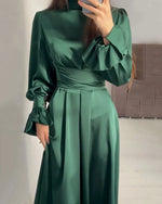 Person wearing a green satin dress with long sleeves in an indoor setting.