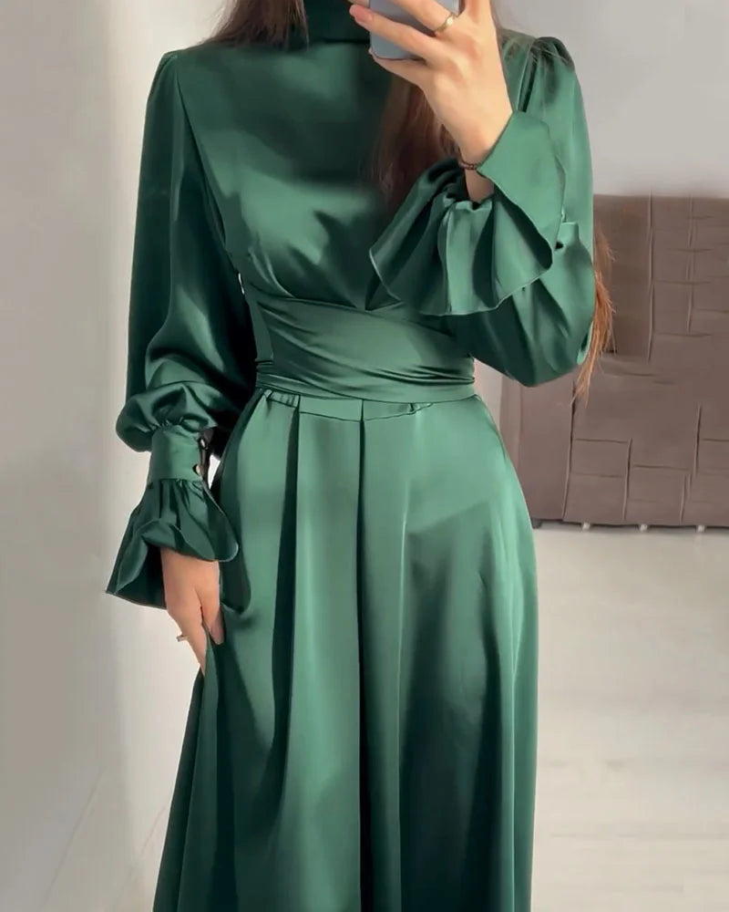 Person wearing a green satin dress with long sleeves in an indoor setting.