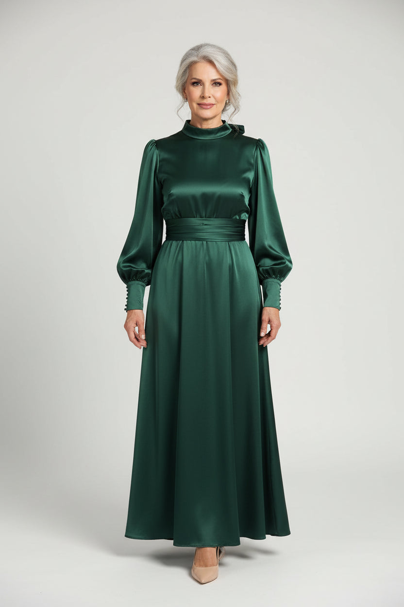 Person wearing a long green dress standing in a room with a sofa and white curtain.