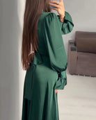 Person wearing a green dress standing in a room with a sofa.