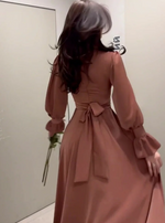Person wearing a long, light brown dress with puffed sleeves in front of a mirror.