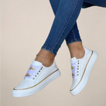 White sneakers with gold accents worn with blue jeans on a beige background
