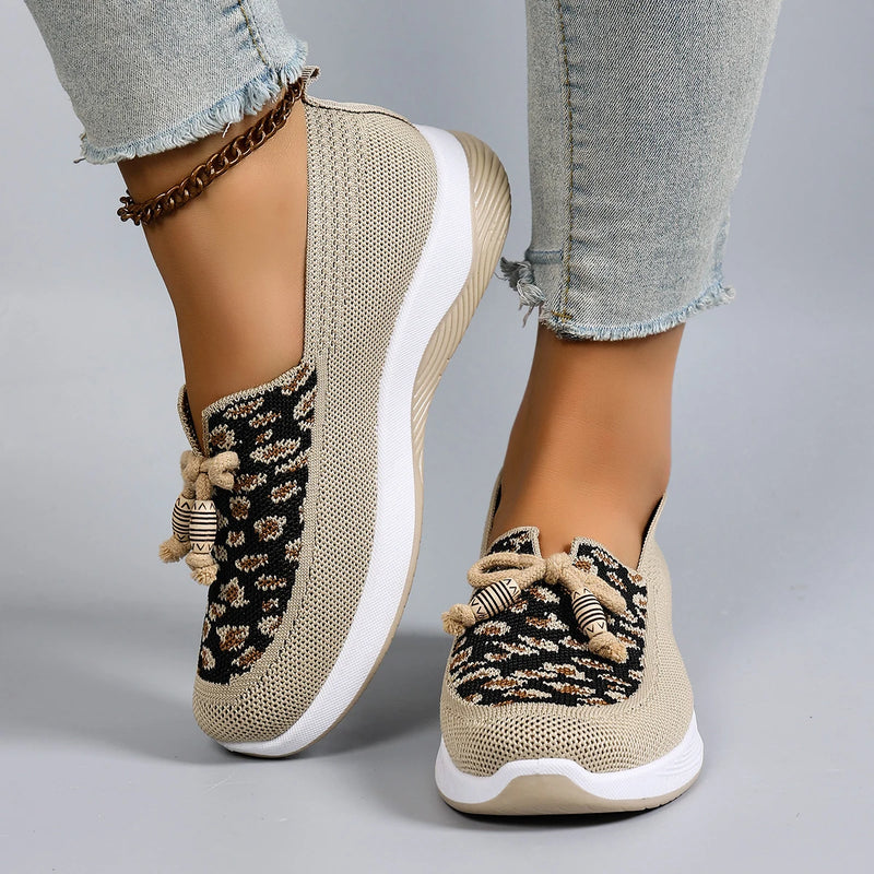 Beige sneakers with black pattern worn by a person on a gray background