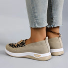 Beige slip-on shoes with white soles worn with light blue jeans on a gray background