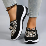 Black slip-on sneakers with leopard print accents worn with light blue jeans on a gray background