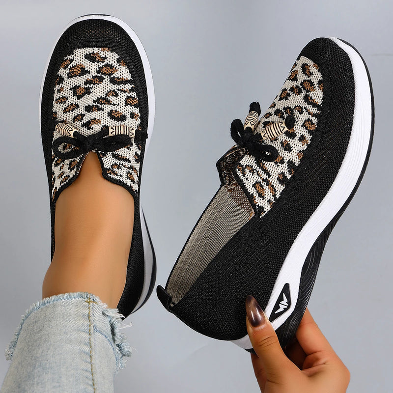 Black slip-on sneakers with leopard print pattern worn by a person on a gray background