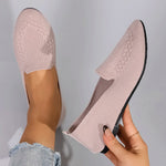Pink knit loafers being held against a gray background