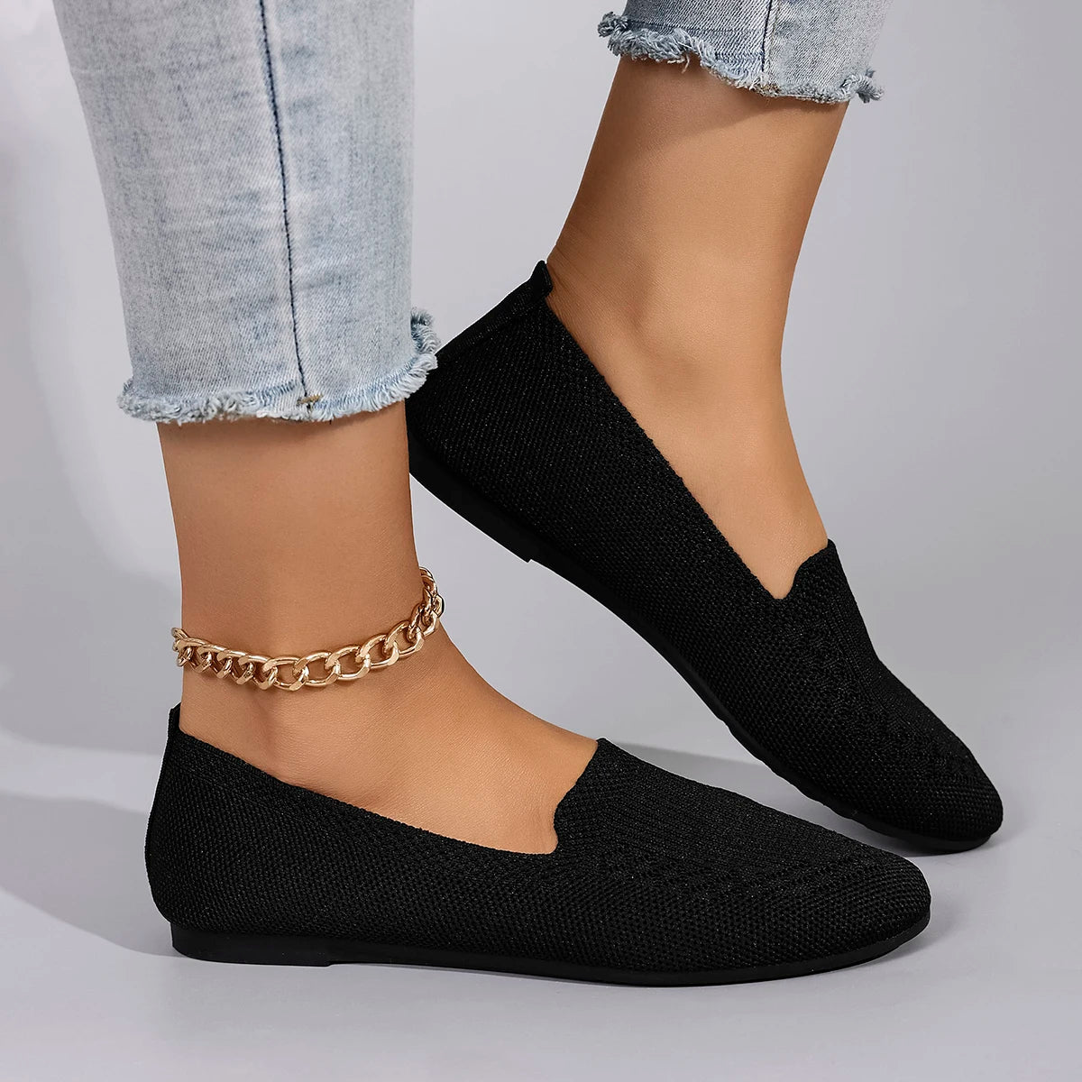 Black knit flats worn with light blue jeans on a neutral background