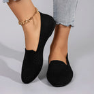 Black slip-on shoes worn with gold anklets on a neutral background