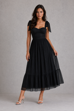 Woman wearing a black dress with bow sleeves against a gray background