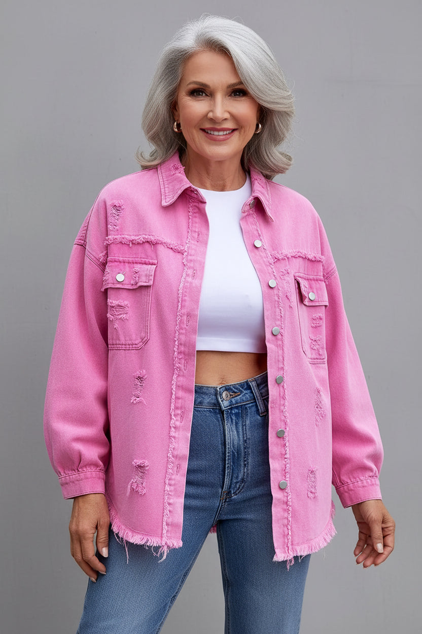 Person wearing a pink distressed denim jacket over a white top and blue jeans on a gray background