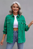 Woman wearing a green denim jacket and blue jeans against a gray background