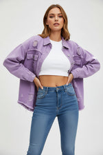 Woman wearing a light purple denim jacket, white top, and blue jeans against a gray background