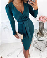 Woman wearing a teal wrap dress in an elegant room with a table and flowers.