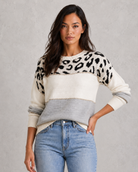 Woman wearing a sweater with leopard print pattern and jeans on a gray background
