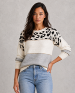 Woman wearing a sweater with leopard print pattern and jeans on a gray background