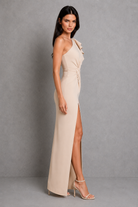 Woman wearing a beige halter neck gown with a slit on a gray background