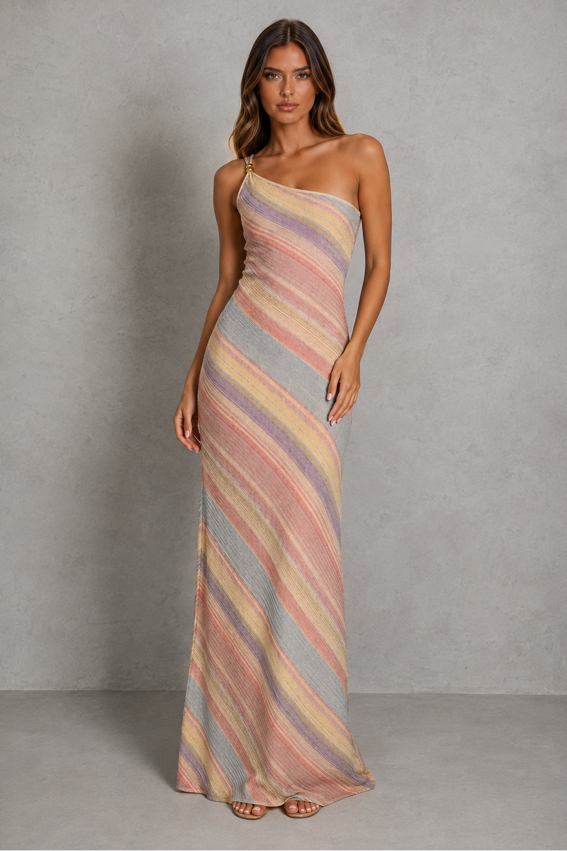 A woman modeling a one-shoulder maxi dress with diagonal pastel stripes in pink, beige, and light blue-gray against a textured gray studio backdrop.