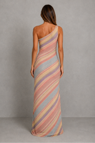 A woman viewed from the back wearing a one-shoulder maxi dress with diagonal pastel stripes in pink, beige, and light blue, set against a neutral gray studio background.