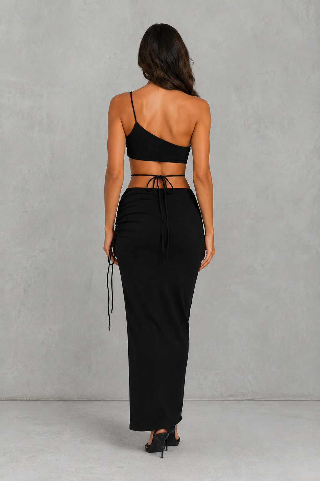 Woman wearing a black strappy top and long black skirt against a gray background