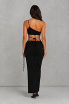 Woman wearing a black strappy top and long black skirt against a gray background