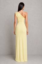 Woman wearing a light yellow one-shoulder gown against a gray background