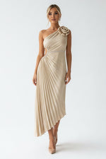 Woman in a beige pleated dress standing in a modern outdoor setting.