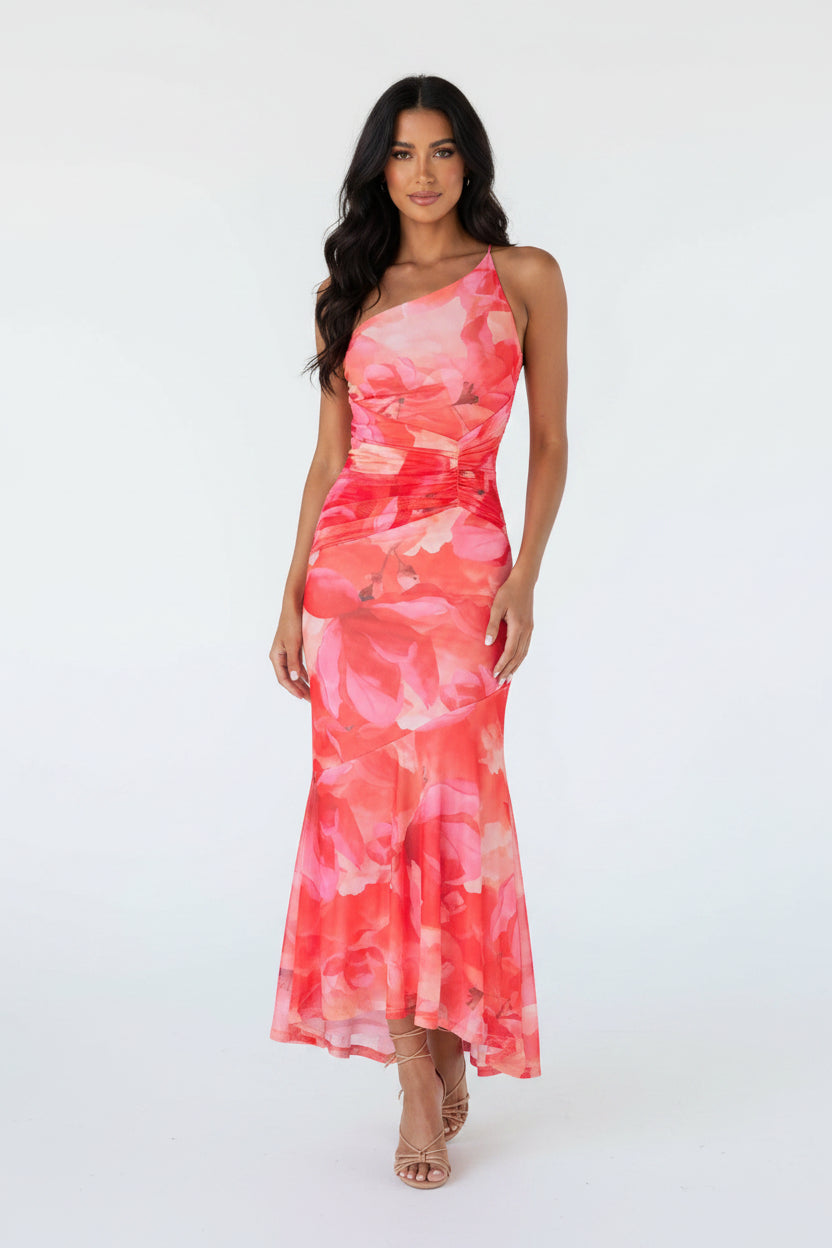 Woman wearing a pink floral dress standing against a gray wall with decorative elements.