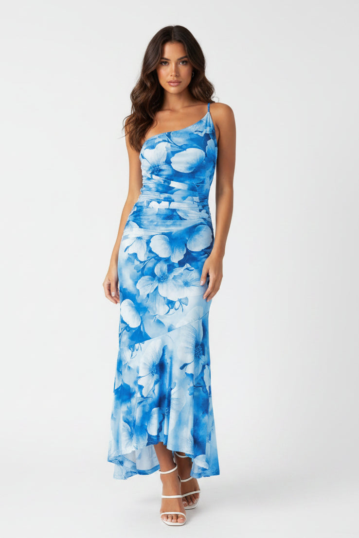 Woman wearing a blue floral dress standing against a gray concrete wall.