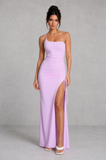 Woman wearing a lavender one-shoulder gown with a high slit on a gray background