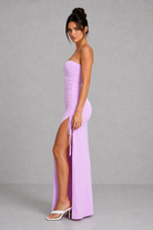 Woman wearing a purple strapless gown with a high slit on a gray background