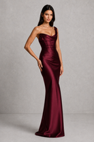 Woman wearing a burgundy one-shoulder gown against a gray background