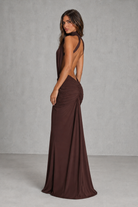 Woman wearing a brown evening gown with a backless design against a gray background