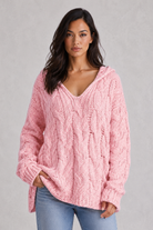 Woman wearing a pink cable knit sweater against a gray background