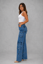 Woman wearing a white top and blue patchwork jeans on a gray background