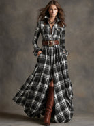Woman wearing a long plaid dress with brown boots against a gray background